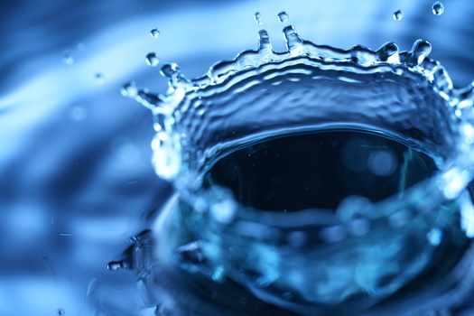 Water droplet impact creating a circular crown splash with bright blue lighting and bokeh background.