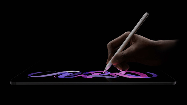 Hand holding a stylus drawing glowing purple and pink brushstrokes on a tablet screen against a black background.