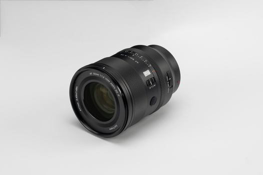 Black telephoto zoom lens with focus ring and depth-of-field scale against neutral gray background.