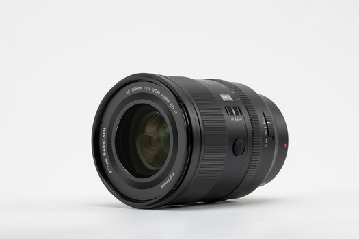 Black telephoto zoom lens with glass elements visible through front barrel, mounted on neutral background.