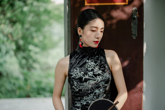 Woman in black patterned sleeveless top with red drop earrings standing in doorway.