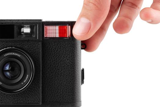 Hand holding a black Lomography instant film camera with red film door open.