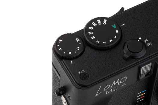 Top view of a rangefinder camera showing two adjustment dials and control buttons on its black leather body.