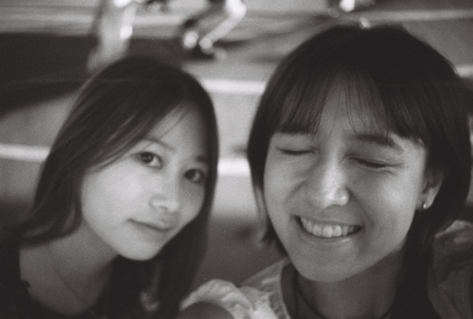 Two young women smiling at the camera in a black and white portrait.