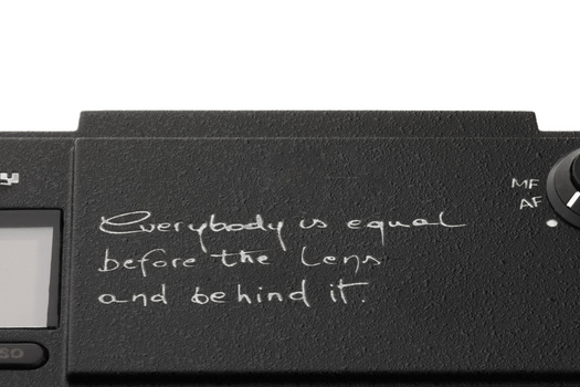 Handwritten text on a camera's LCD screen protector or surface reads "everybody is equal before the lens and behind it."