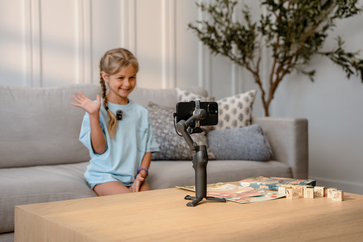Young child waving at smartphone mounted on tripod with gimbal stabilizer during content creation.