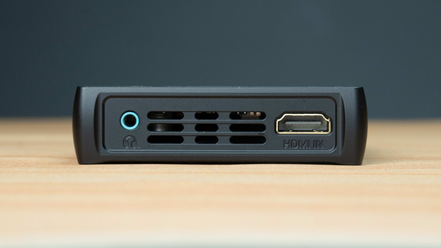 Front panel of a black media device with ventilation grilles, a power button, and an HDMI port on a wooden surface.