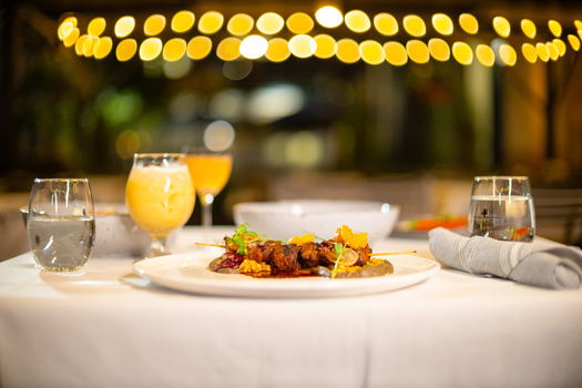 Plated dish with roasted vegetables and protein on white tablecloth with golden bokeh lights overhead.