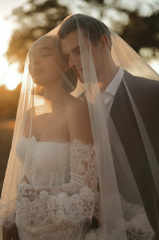 Bride and groom embracing under veil during golden hour sunset.
