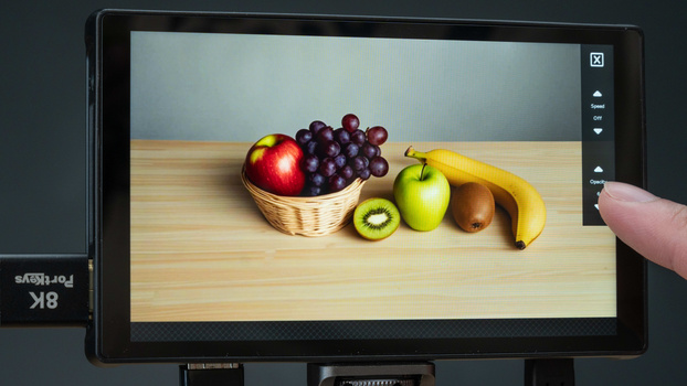 Monitor displaying a still life composition of fresh fruits arranged on a wooden surface.