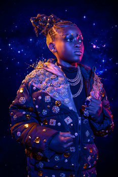 Portrait of a person wearing an ornate, embellished jacket against a deep blue starry background.