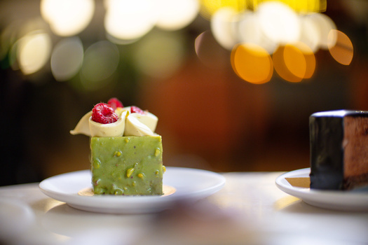 Pistachio-green layered dessert topped with raspberry and white chocolate garnish on white plate.