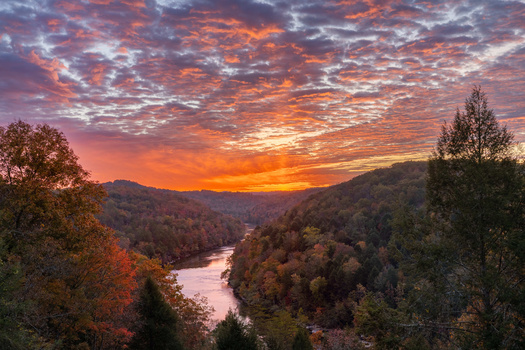 River valley at sunset with forested hillsides under a dramatic orange and purple sky.