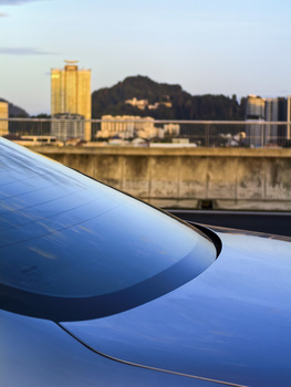 Blue car hood in sharp focus with urban cityscape and river across blurred background at dusk.