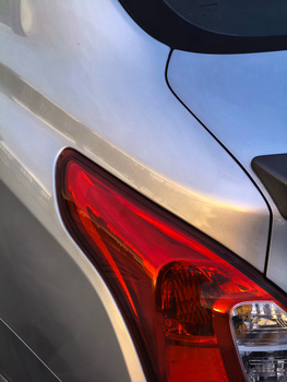 Close-up of a white car's rear quarter panel and taillight in bright daylight.