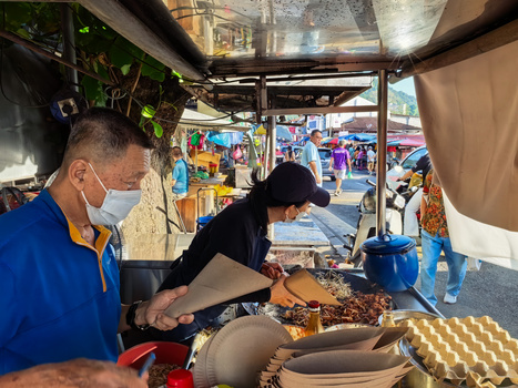 Food vendor preparing grilled meat at an outdoor market stall during daytime.
