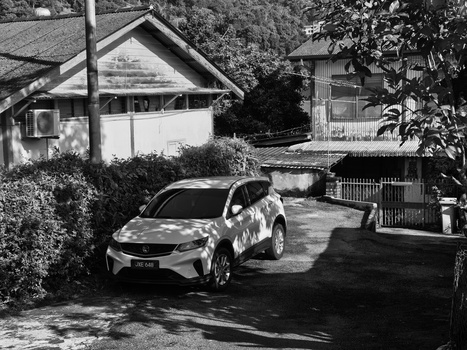 Modern SUV parked in residential driveway with houses and landscaping in black and white.