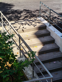 Metal stair railing casting intricate shadows on concrete steps in bright sunlight.