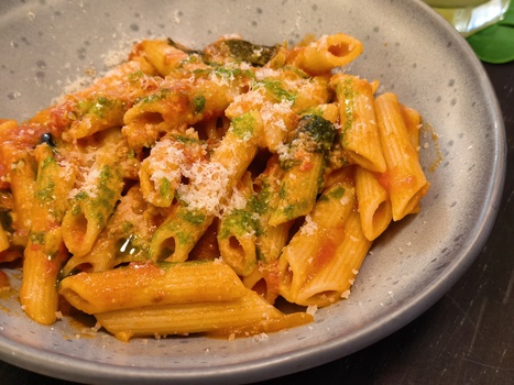 Penne pasta with green pesto, grated cheese, and fresh herbs served in a speckled gray bowl.