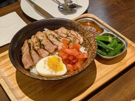 Bowl of ramen with sliced pork, soft-boiled egg, tomato, and sprouts on wooden serving board.