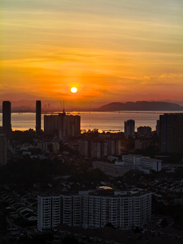 Golden sunset over a coastal city skyline with high-rise buildings silhouetted against an orange sky and calm water.