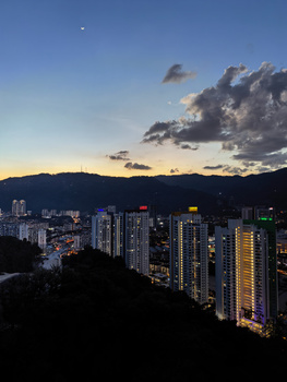 Cityscape at dusk with illuminated high-rise buildings against twilight sky and mountains.