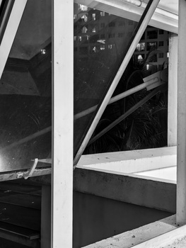 Black and white photograph of a storefront window with white framing and reflective glass, creating geometric patterns and depth.