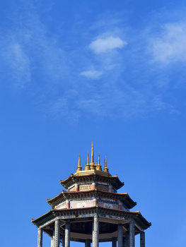 Multi-tiered ornamental tower with golden spires against clear blue sky.