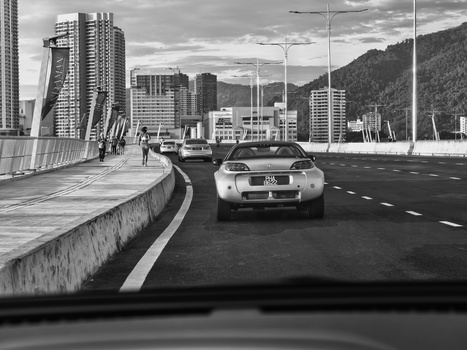 Silver car driving on a multi-lane highway with mountains and city buildings visible in the background.