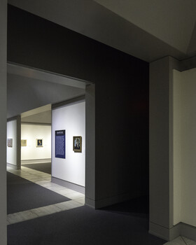 Gallery doorway with dark frame revealing white interior walls displaying framed artwork.