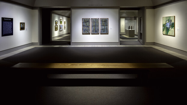 Museum gallery interior with illuminated artwork displays on white walls and a dark floor with central display case.