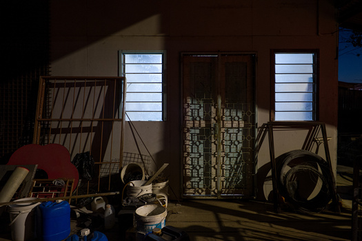 Studio interior with dramatic window light casting shadows across a cluttered floor with equipment and props.
