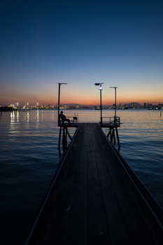 Wooden pier extending into calm water at twilight with city lights reflected on the surface.