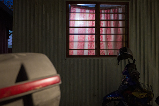 Motorcycle parked in front of an industrial corrugated metal building with a neon pink-lit window at night.