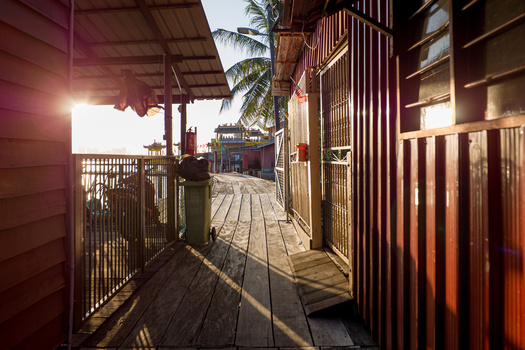 Wooden boardwalk corridor with metal railings, strong backlighting creating deep shadows and warm golden tones.