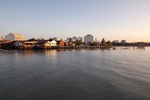 Waterfront neighborhood at golden hour with historic buildings on stilts reflected in calm water.