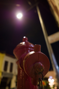Red fire hydrant at night with bright moon and urban building in soft focus background.