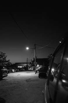 Vehicle parked in dark lot at night with street lamp and utility pole illuminated in background.