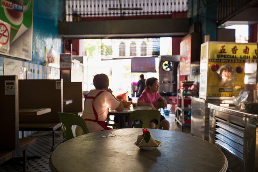 Interior of a busy Asian restaurant with diners seated at tables, natural light streaming through storefront windows, and staff visible in the background.