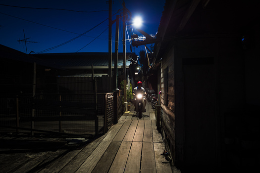 Nighttime alley with wooden boardwalk lit by overhead lights and moonlight.