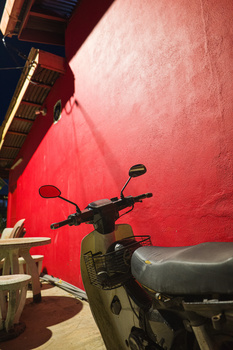 Motorcycle parked in front of a large red fabric backdrop or sail in bright sunlight.
