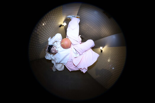 Overhead view of a person in light blue and pink clothing holding a basketball on a brick floor.