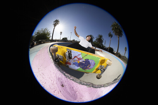 Skateboarder performing trick in concrete bowl with fish-eye lens distortion.