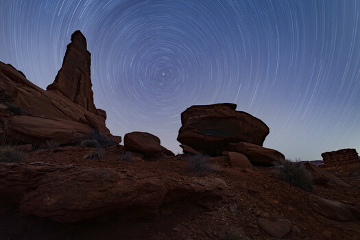 Desert rock formations silhouetted against a night sky with concentric star trail circles.