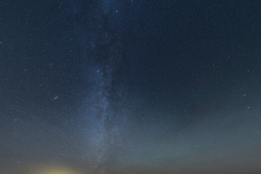 Milky Way galaxy stretching across a dark night sky above a hazy horizon.