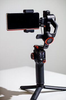 Three-axis gimbal stabilizer with smartphone mount and control handle against white background.