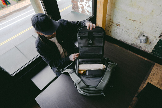 Photographer opening a black camera backpack near a doorway, revealing organized interior compartments and gear storage.