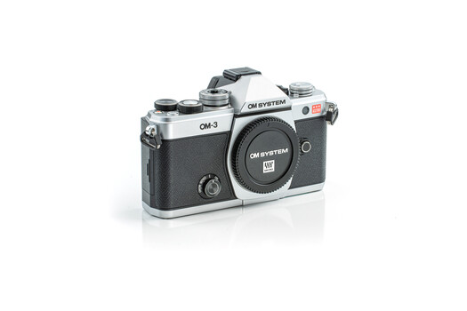 OM System OM-3 film camera with chrome and black body showing top plate and lens.