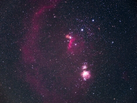 Deep-space astrophotography showing Orion Nebula region with bright pink emission nebulae and scattered stars.