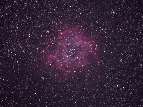 Pink nebula surrounded by stars against dark purple night sky.